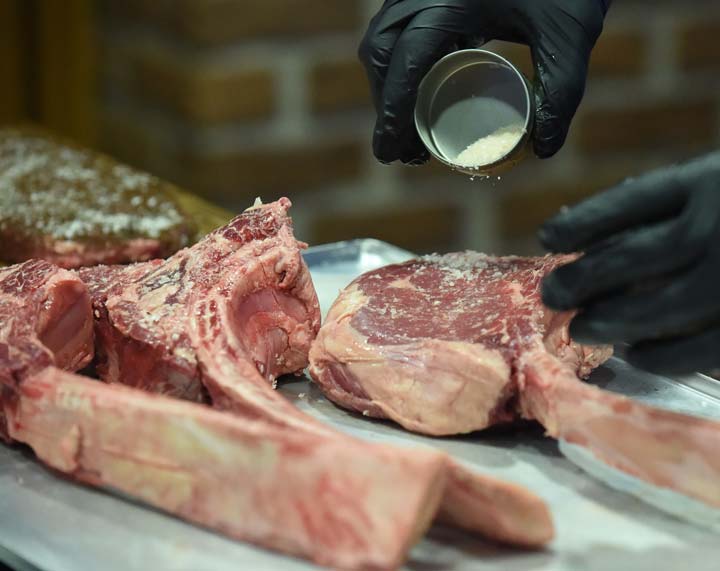 Fleischer bestreut Fleisch aus eigener Herstellung mit Gewürzen.